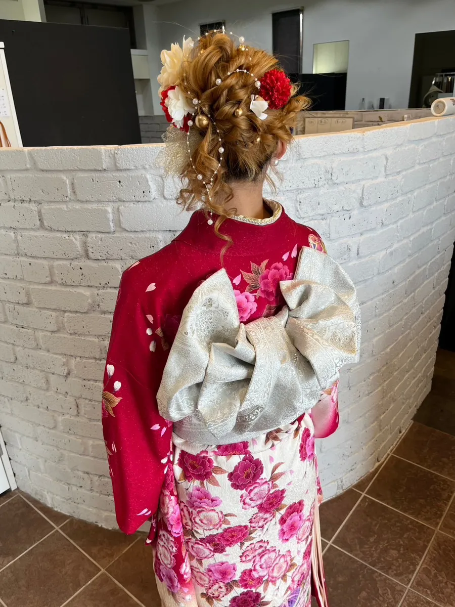 振袖の着付けとヘアセットの後ろ姿。赤とピンクの花柄の振袖に銀の帯