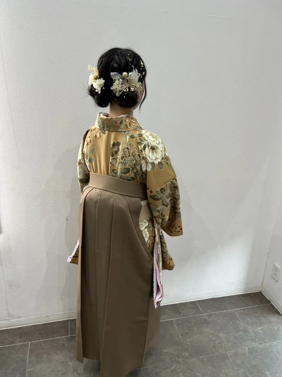袴の着付けとヘアセットの後ろ姿。金茶の花柄の着物に茶の袴